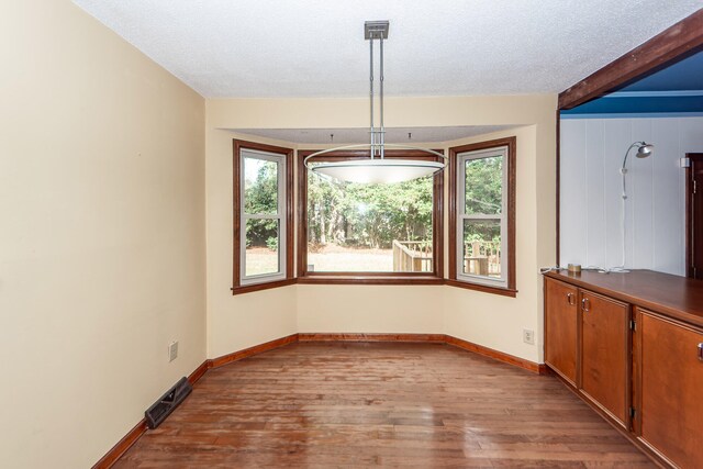 unfurnished dining area with beamed ceiling, a textured ceiling, and light wood-type flooring