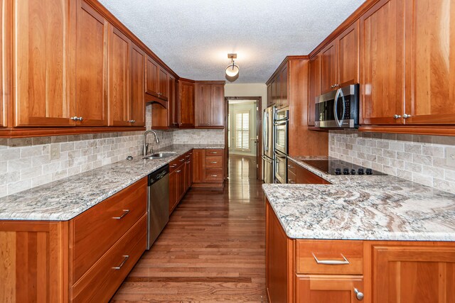 kitchen with stainless steel appliances, sink, light stone counters, tasteful backsplash, and wood-type flooring