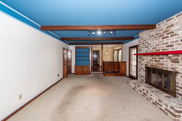 unfurnished living room with a brick fireplace, beamed ceiling, carpet flooring, and track lighting