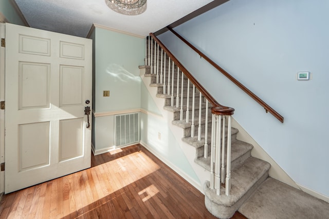 foyer featuring a textured ceiling, hardwood / wood-style flooring, ornamental molding, and vaulted ceiling