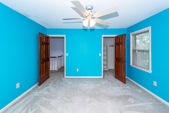 unfurnished bedroom featuring ceiling fan, light carpet, a closet, and a walk in closet