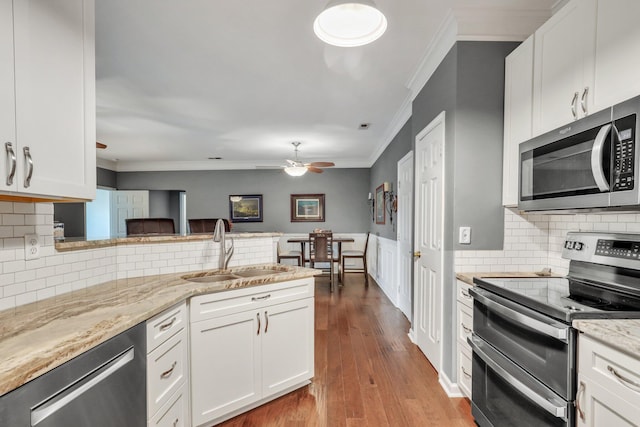 kitchen featuring crown molding, dark wood-type flooring, a peninsula, stainless steel appliances, and a sink