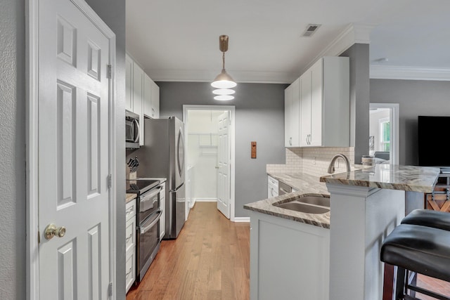 kitchen with decorative light fixtures, appliances with stainless steel finishes, light hardwood / wood-style floors, kitchen peninsula, and a breakfast bar area