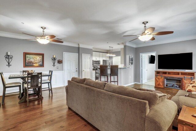 living room with a glass covered fireplace, crown molding, wood finished floors, and ceiling fan