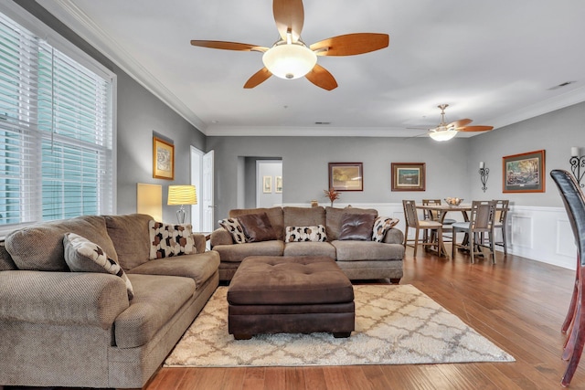 living area with a ceiling fan, wood finished floors, visible vents, and ornamental molding