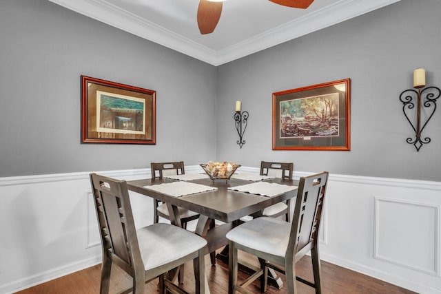 dining area with a ceiling fan, wood finished floors, a wainscoted wall, and ornamental molding