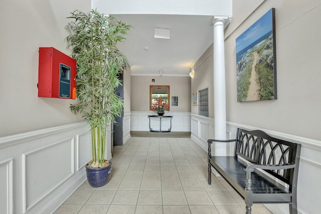 hallway with light tile patterned floors, ornamental molding, wainscoting, and decorative columns