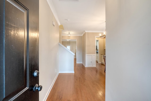 corridor featuring an inviting chandelier, baseboards, ornamental molding, and wood finished floors