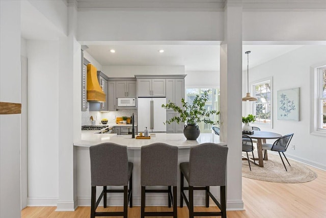 kitchen featuring gray cabinets, premium range hood, tasteful backsplash, light hardwood / wood-style floors, and white appliances