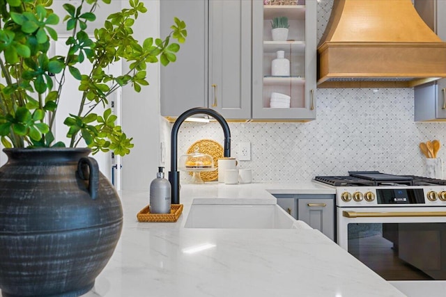 details with sink, gray cabinetry, light stone counters, range with gas stovetop, and custom range hood