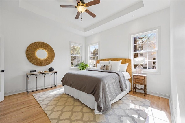 bedroom with a tray ceiling, ceiling fan, and light wood-type flooring