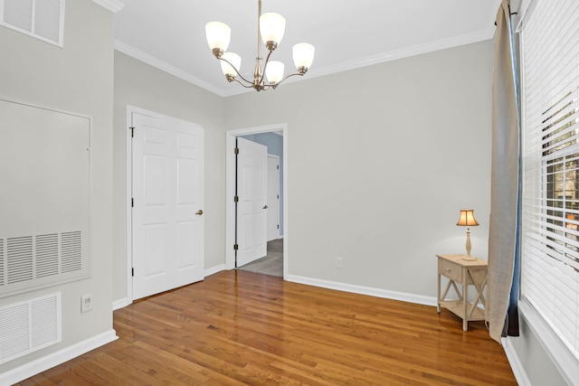 spare room featuring crown molding, hardwood / wood-style flooring, and a notable chandelier