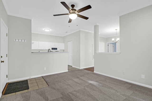 unfurnished living room featuring dark tile patterned floors, ceiling fan with notable chandelier, and crown molding