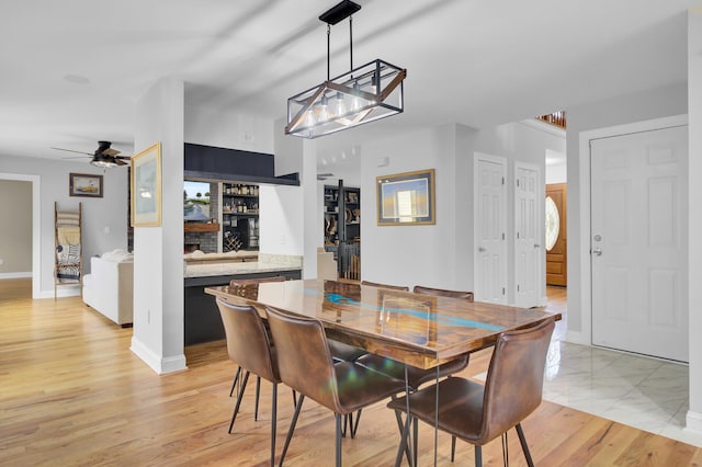 dining space featuring a dry bar, light wood-style flooring, baseboards, and ceiling fan