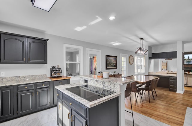 kitchen with a breakfast bar, light stone countertops, black electric cooktop, and a center island