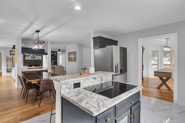 kitchen featuring a center island, pendant lighting, light stone countertops, stainless steel fridge with ice dispenser, and black electric cooktop