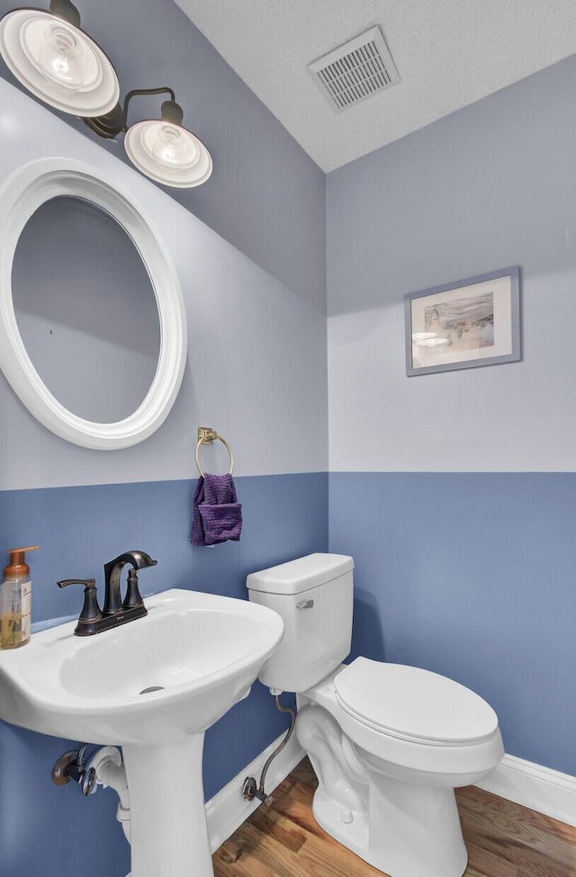 half bathroom featuring toilet, baseboards, visible vents, and wood finished floors