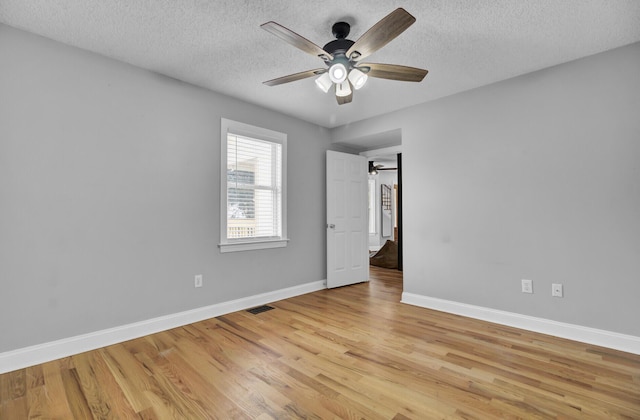 empty room featuring visible vents, light wood-style floors, a ceiling fan, a textured ceiling, and baseboards