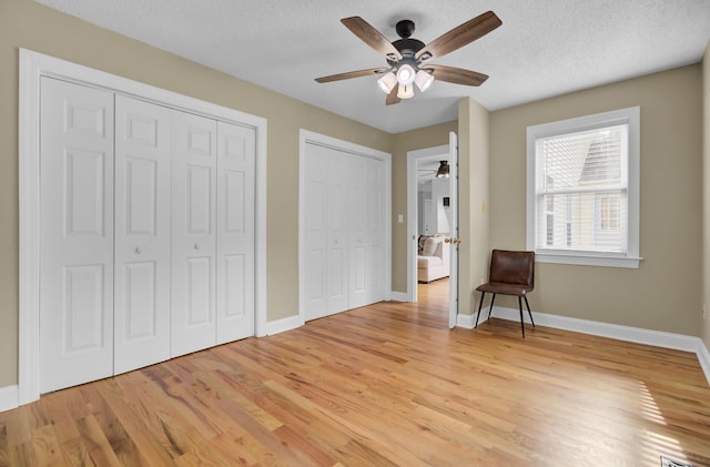 unfurnished bedroom featuring light wood-type flooring, a textured ceiling, baseboards, and multiple closets