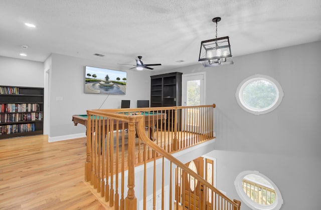 hallway featuring light wood finished floors, baseboards, a textured ceiling, an upstairs landing, and recessed lighting