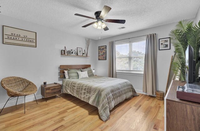 bedroom featuring a ceiling fan, visible vents, a textured ceiling, and light wood finished floors