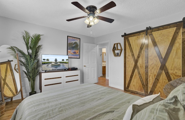 bedroom featuring a barn door, a textured ceiling, a ceiling fan, and wood finished floors