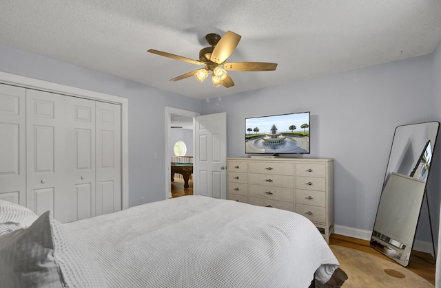 bedroom featuring ceiling fan, a textured ceiling, wood finished floors, baseboards, and a closet