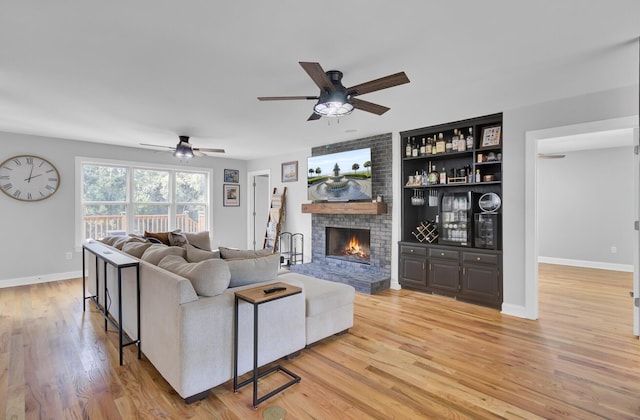 living room with a fireplace, light wood-style flooring, baseboards, and ceiling fan