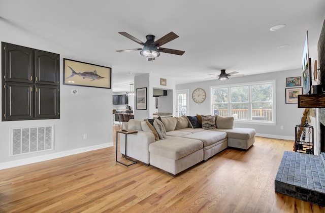 living area featuring light wood finished floors, visible vents, a fireplace with raised hearth, a ceiling fan, and baseboards