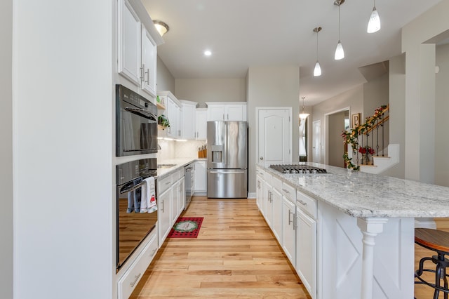 kitchen with light hardwood / wood-style flooring, appliances with stainless steel finishes, white cabinetry, a kitchen bar, and decorative light fixtures