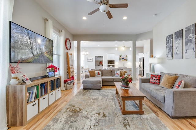 living room with ceiling fan with notable chandelier and light wood-type flooring