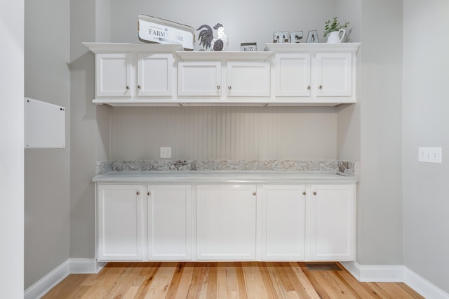 bar with white cabinetry, light stone countertops, and light hardwood / wood-style floors