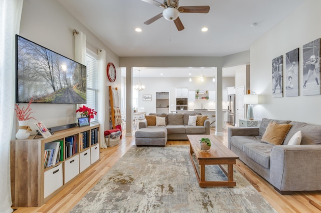 living room featuring ceiling fan with notable chandelier and light hardwood / wood-style floors