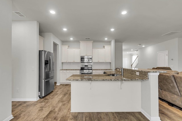 9998 Winged Elm St, Ladson, SC 29456 - kitchen featuring appliances with stainless steel finishes, a kitchen breakfast bar, a sink, light wood-type flooring, and stone counters