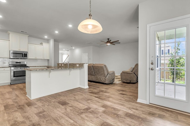 9998 Winged Elm St, Ladson, SC 29456 - kitchen with stainless steel appliances, a breakfast bar area, open floor plan, light stone counters, and light wood-style flooring