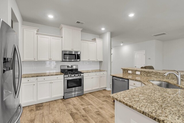 9998 Winged Elm St, Ladson, SC 29456 - kitchen with stainless steel appliances, a sink, decorative backsplash, white cabinetry, and light wood-style floors