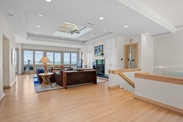 living room with a tray ceiling, ornamental molding, a skylight, and light wood-type flooring