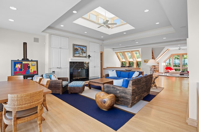 living room featuring ceiling fan, light wood-type flooring, a fireplace, and a raised ceiling