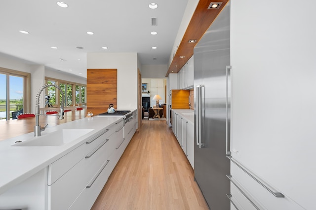 kitchen with appliances with stainless steel finishes, sink, white cabinetry, and light hardwood / wood-style floors