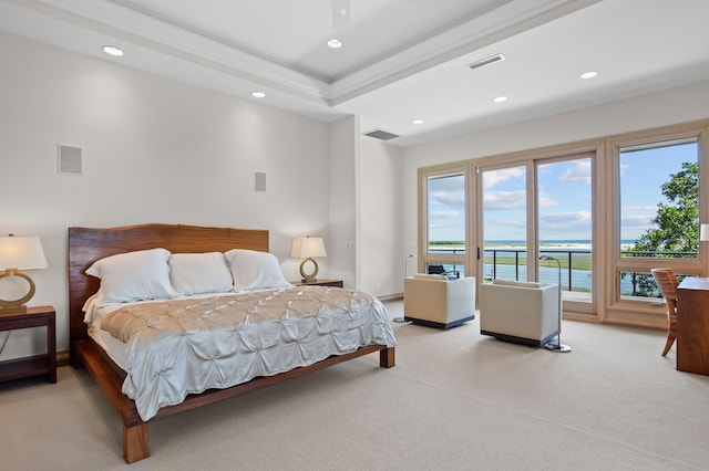 carpeted bedroom featuring a tray ceiling and a water view