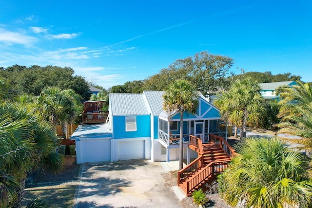 beach home with concrete driveway, metal roof, an attached garage, and stairs