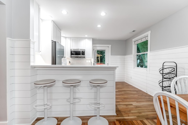 kitchen featuring a wainscoted wall, a peninsula, wood finished floors, white cabinetry, and appliances with stainless steel finishes