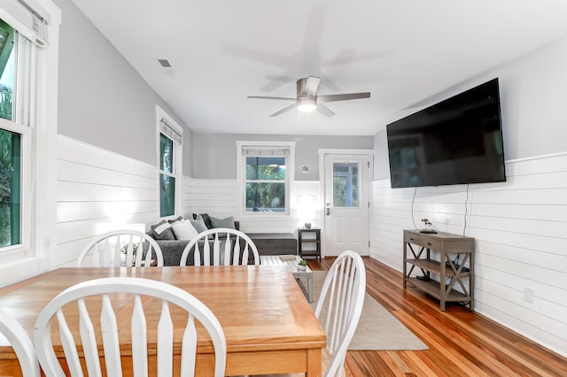 dining area with a wainscoted wall, light wood-style flooring, and a ceiling fan