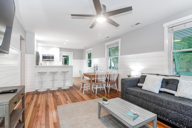 living area featuring hardwood / wood-style flooring, visible vents, a wealth of natural light, and a wainscoted wall