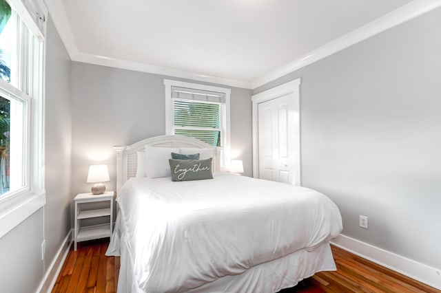 bedroom with ornamental molding, a closet, wood finished floors, and baseboards