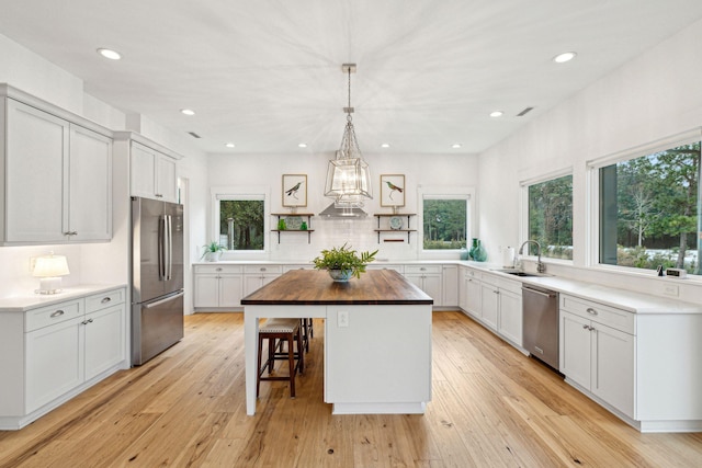 kitchen with open shelves, appliances with stainless steel finishes, light wood-type flooring, and butcher block counters