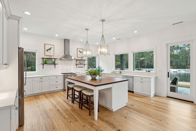 kitchen featuring open shelves, butcher block countertops, a sink, appliances with stainless steel finishes, and wall chimney exhaust hood