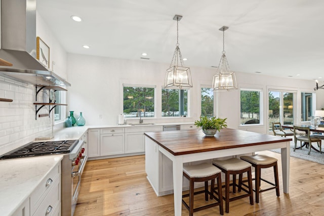 kitchen featuring a sink, wooden counters, light wood-type flooring, high end range, and wall chimney exhaust hood