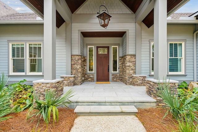 doorway to property featuring stone siding, a shingled roof, and covered porch