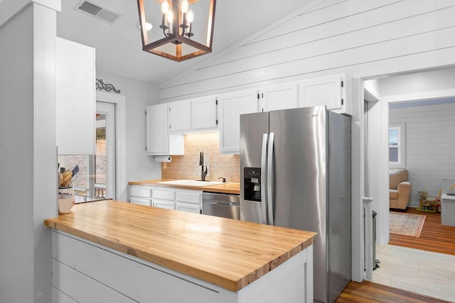 kitchen featuring sink, vaulted ceiling, hanging light fixtures, stainless steel appliances, and white cabinets